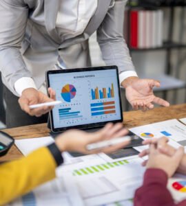 A woman is showing a tablet to two other women. The tablet has a pie chart on it
