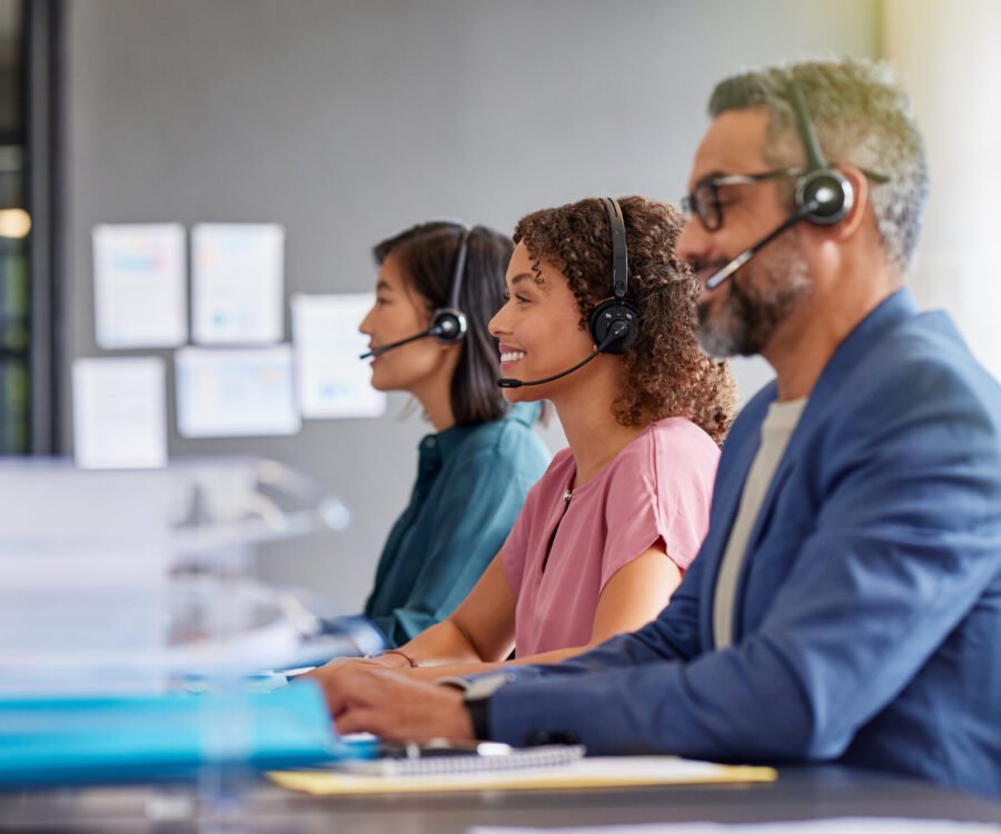 Professional customer service representatives focused on their computers in a modern office. Call center mixed race agents wearing headsets and providing assistance to clients in remote. Dedicated support team members working efficiently in a call center.